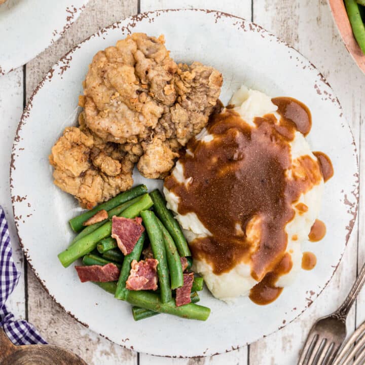 close up of a venison cutlet on a plate with mashed potatoes and gravy and green beans