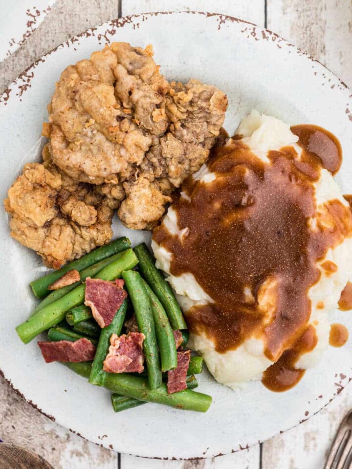 close up of a venison cutlet on a plate with mashed potatoes and gravy and green beans