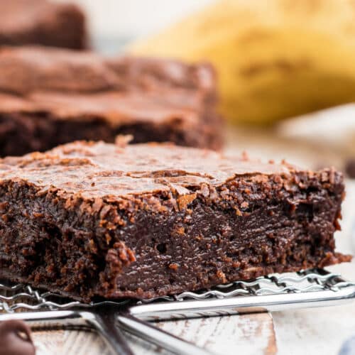 a close up of a moist banana brownie with a banana in the background