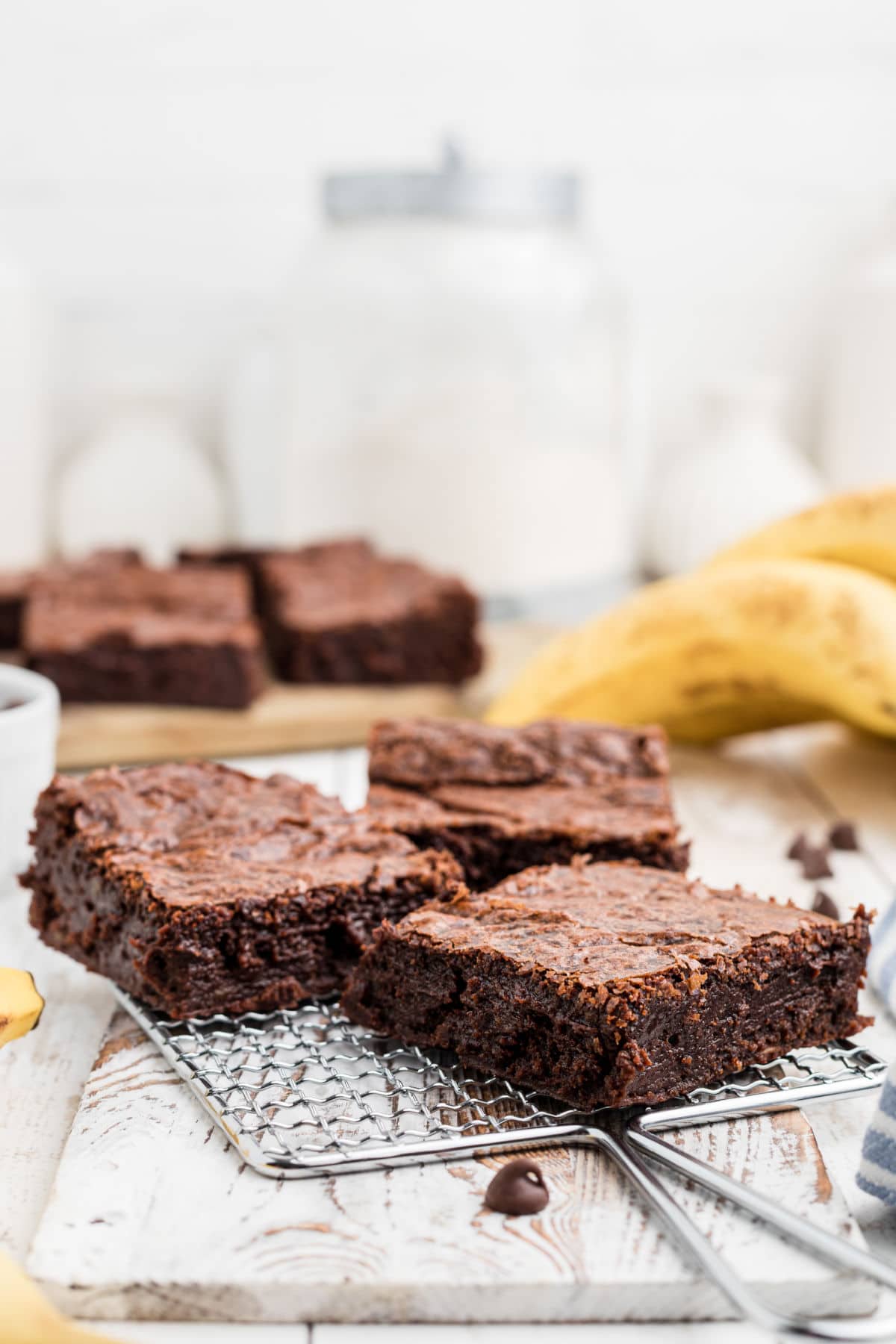 a small rack holding three banana brownies with a few bananas in the background