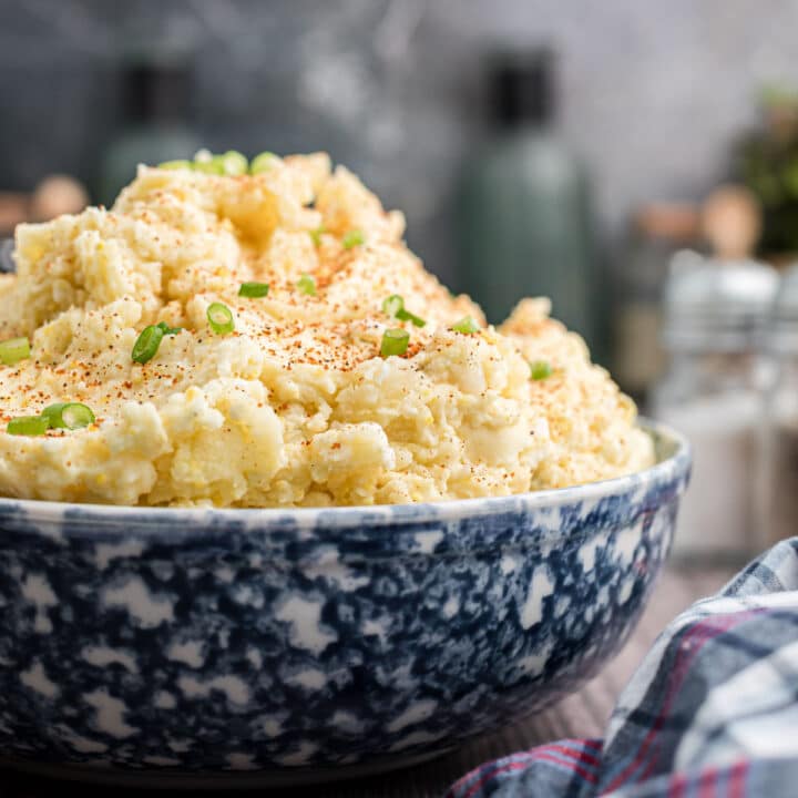 a close up image of a large bowl of Cajun potato salad with green onions sprinkled on top