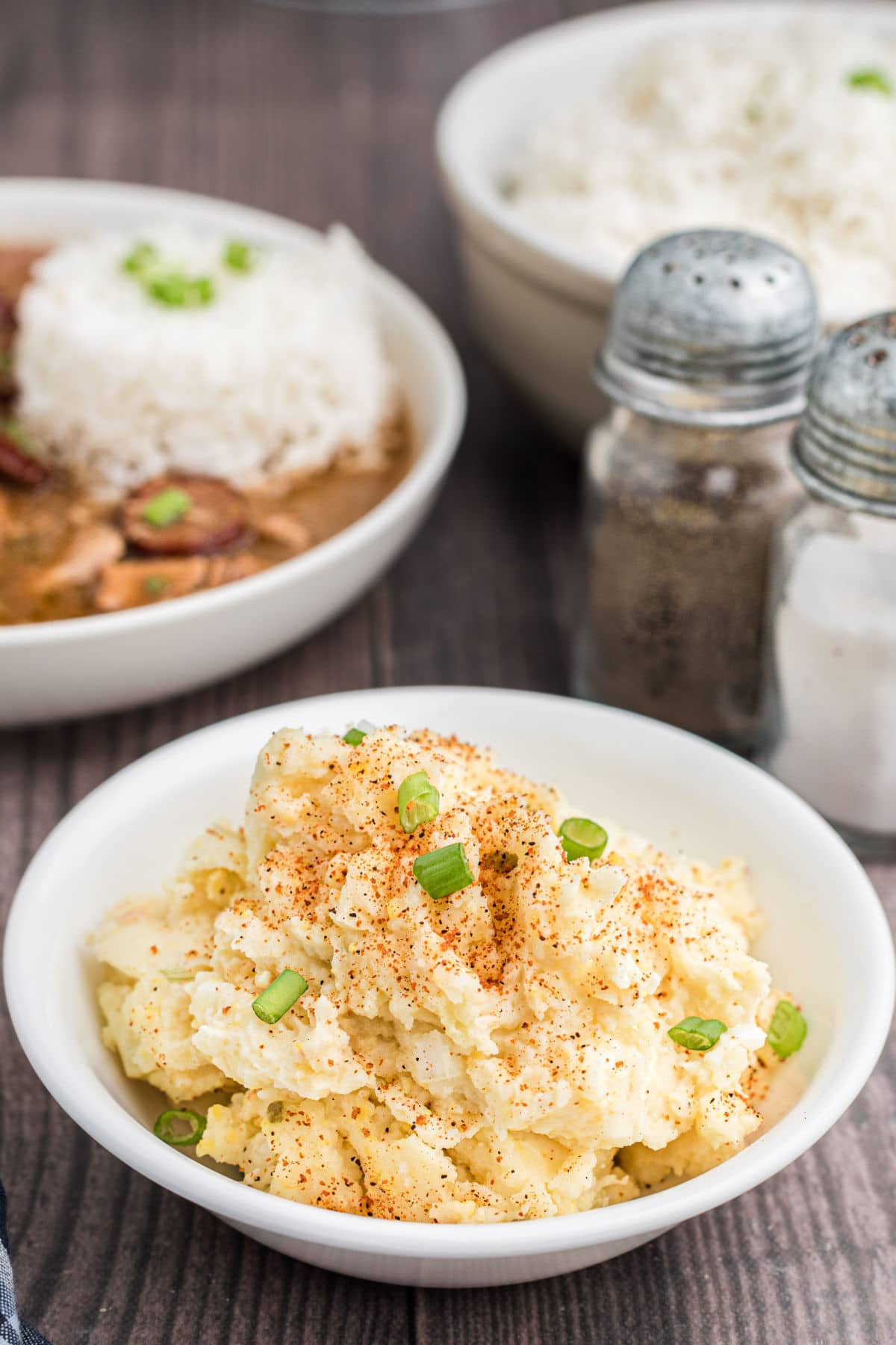 a bowl of cajun potato salad with gumbo in the background