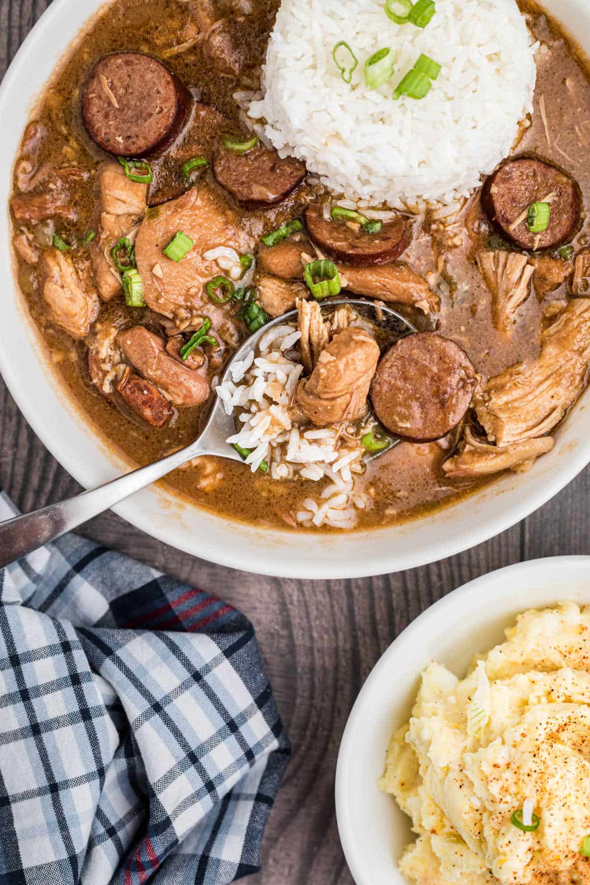 a bowl of chicken sausage gumbo with a spoon hanging out of it with rice in the middle, a potato salad on the side