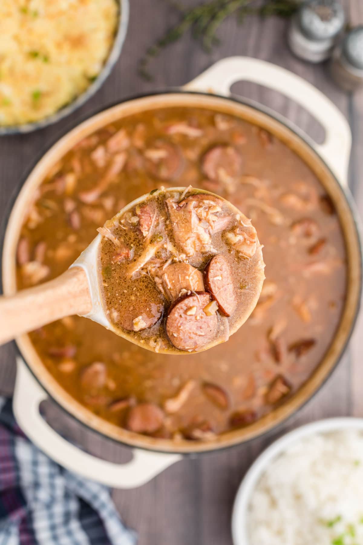 a ladle of chicken and sausage gumbo held up to the camera with the pot of gumbo beneath