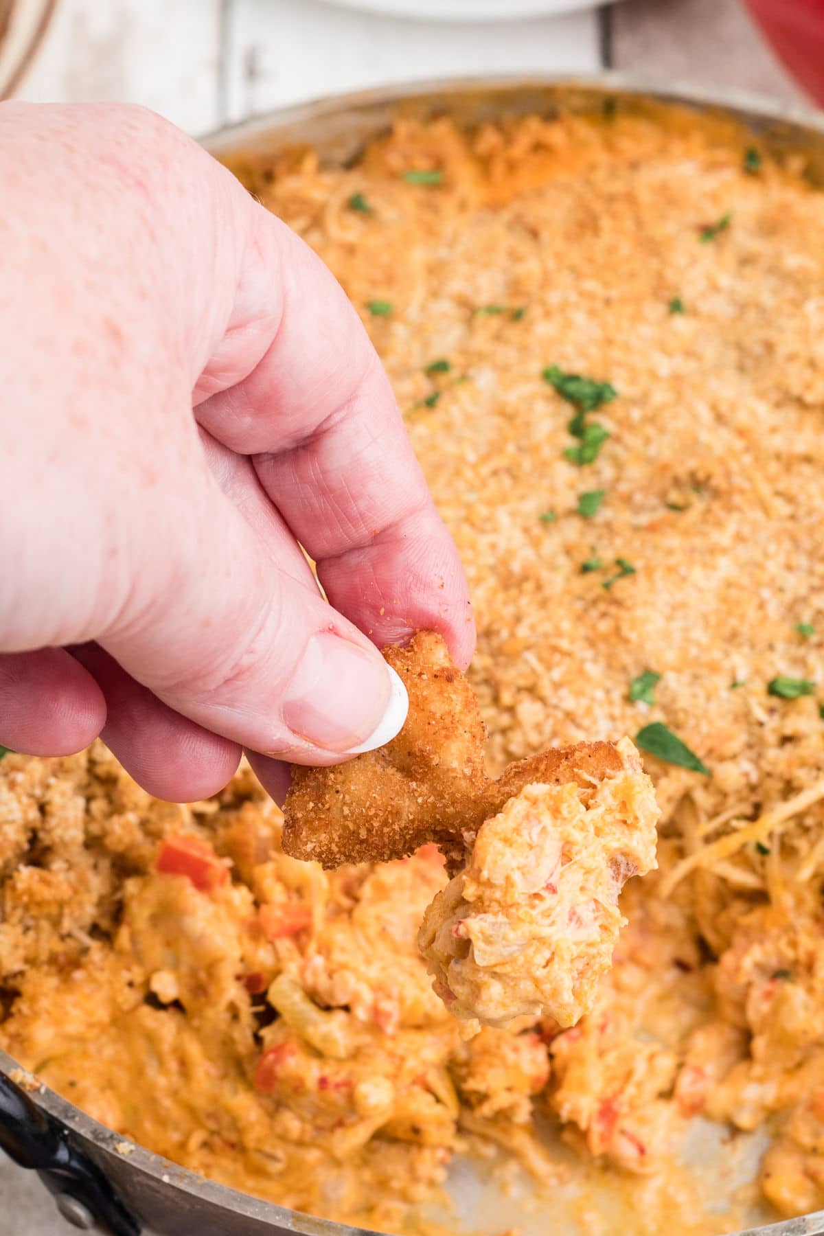 a close up picture of a hand dipping a fried bowtie pasta chip into crawfish dip