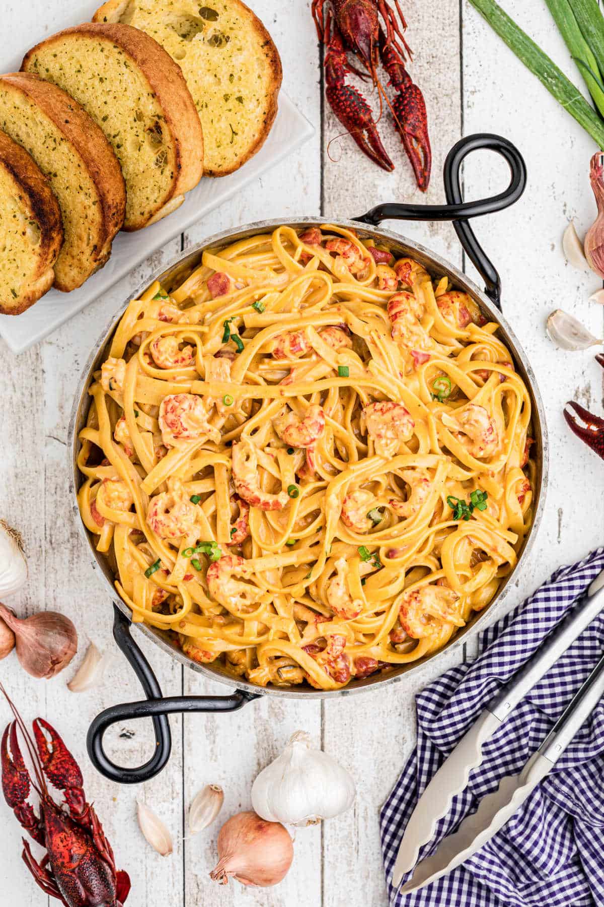 overhead view of crawfish fettuccine in a skillet with boiled crawfish and garlic and texas toast arranged around