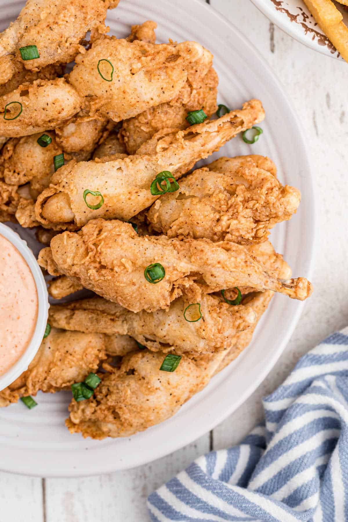 close up view of a plate of fried frog legs with a small bowl of dip poking in