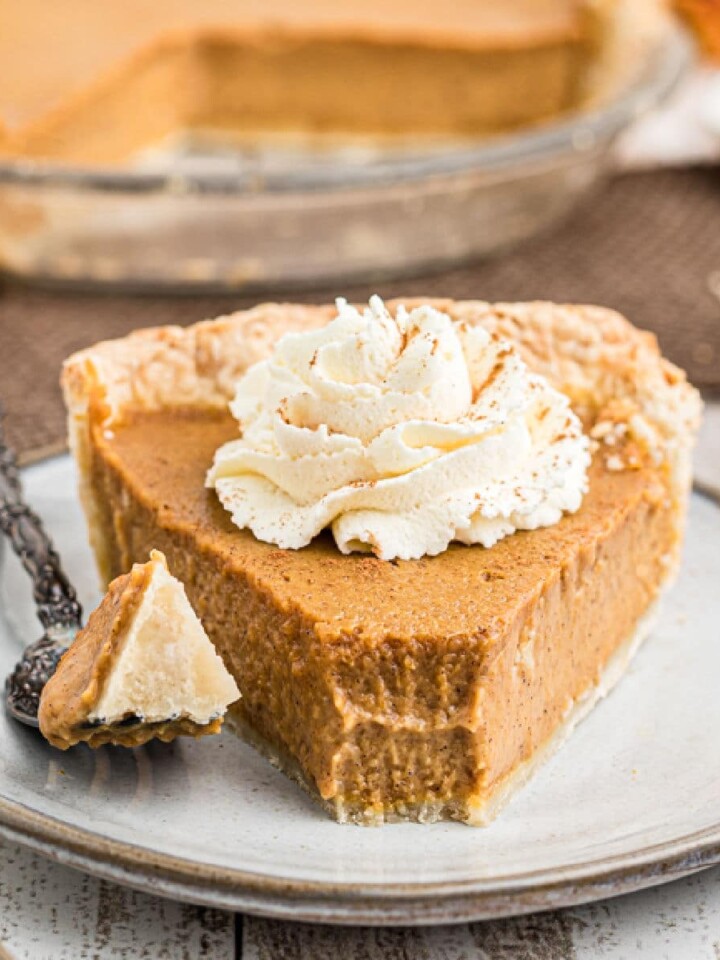 close up of an Amish pumpkin pie with a fork having just taken a piece from the front of the pie - a dollop of cream on top