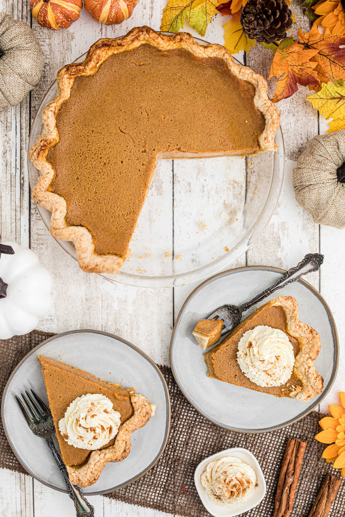 overhead shot of an Amish Pumpkin Pie with two pieces cut out of it on plates with forks and a dollop of cream on top of each