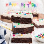 a close up of a stack of birthday brownies, three of them, with a set of happy birthday candles in the background