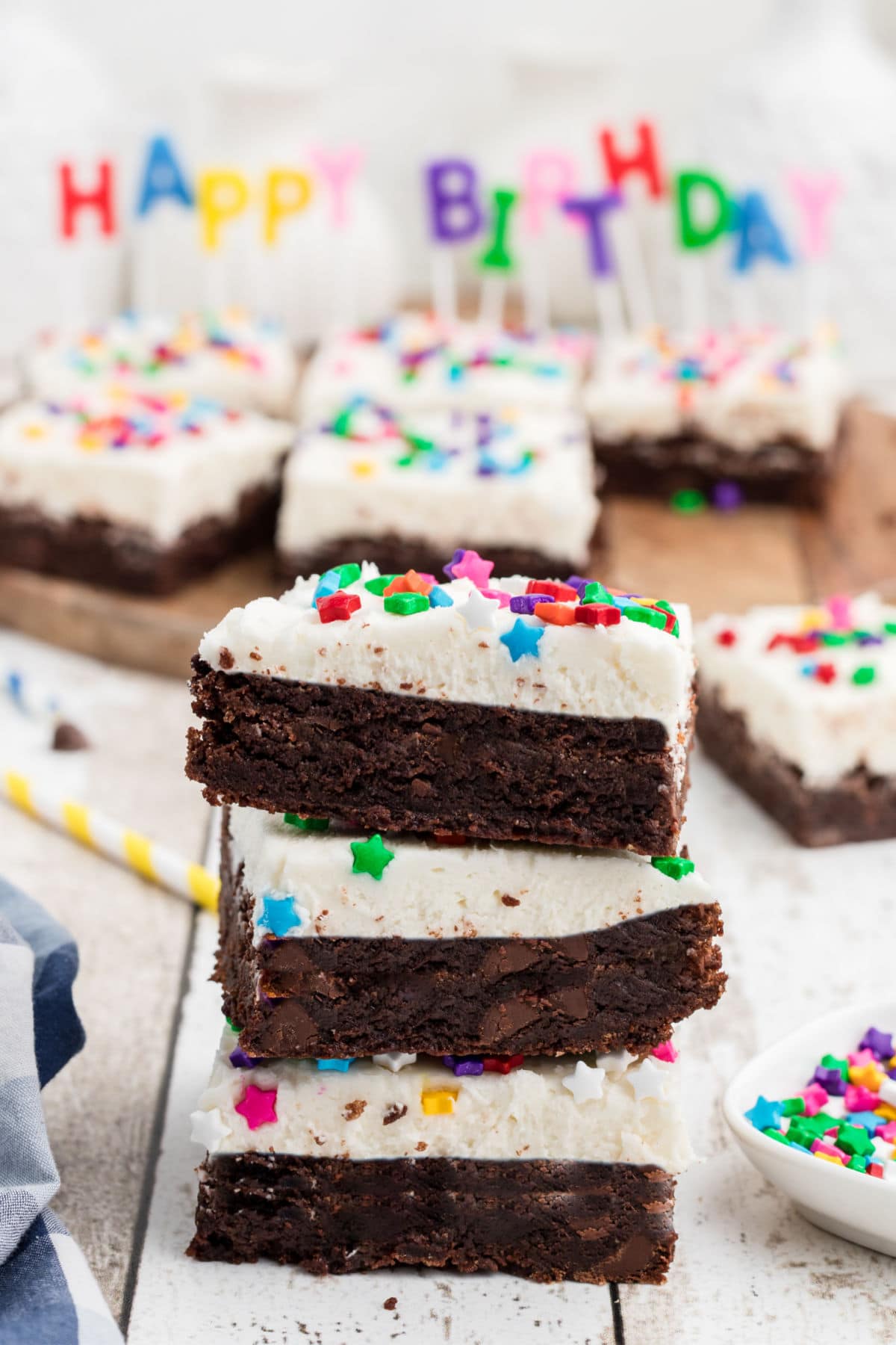 a stack of 3 birthday brownies, with frosting. A set of happy birthday candles in the background.