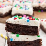 a stack of birthday brownies with buttermilk frosting with sprinkles with happy birthday candles in the background