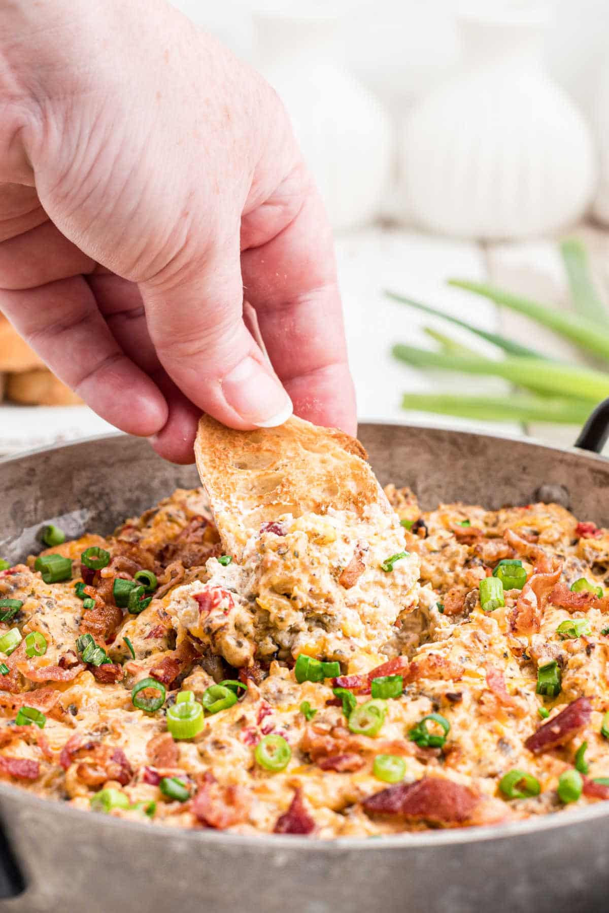 a skillet with some boudin dip cooked and some green onions sprinkled on top with a hand dipping into the dip