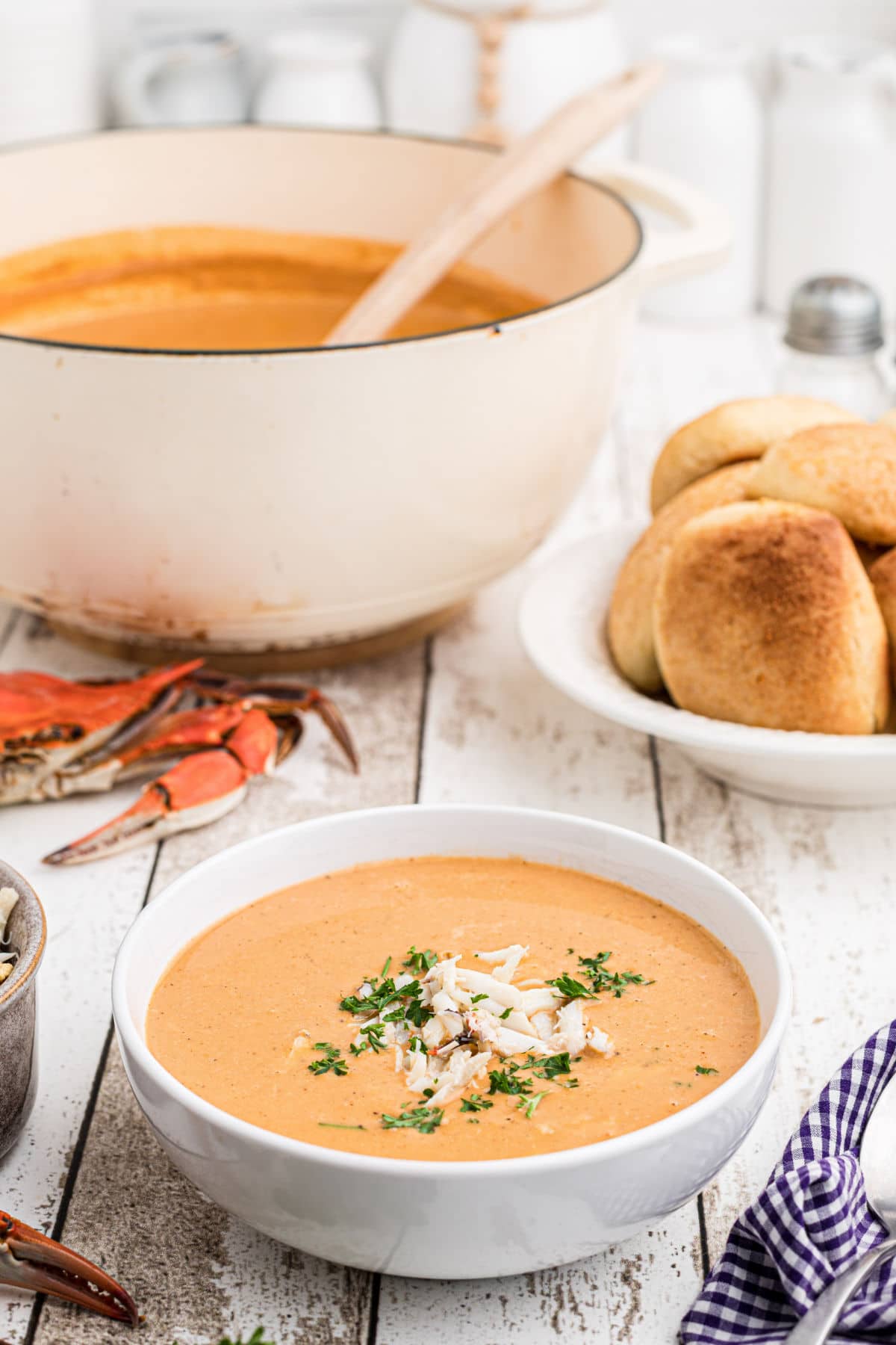 a bowl full of crab soup with a pot in the background and a boiled crab - the bowl of crab soup has crab meat sprinkled on top