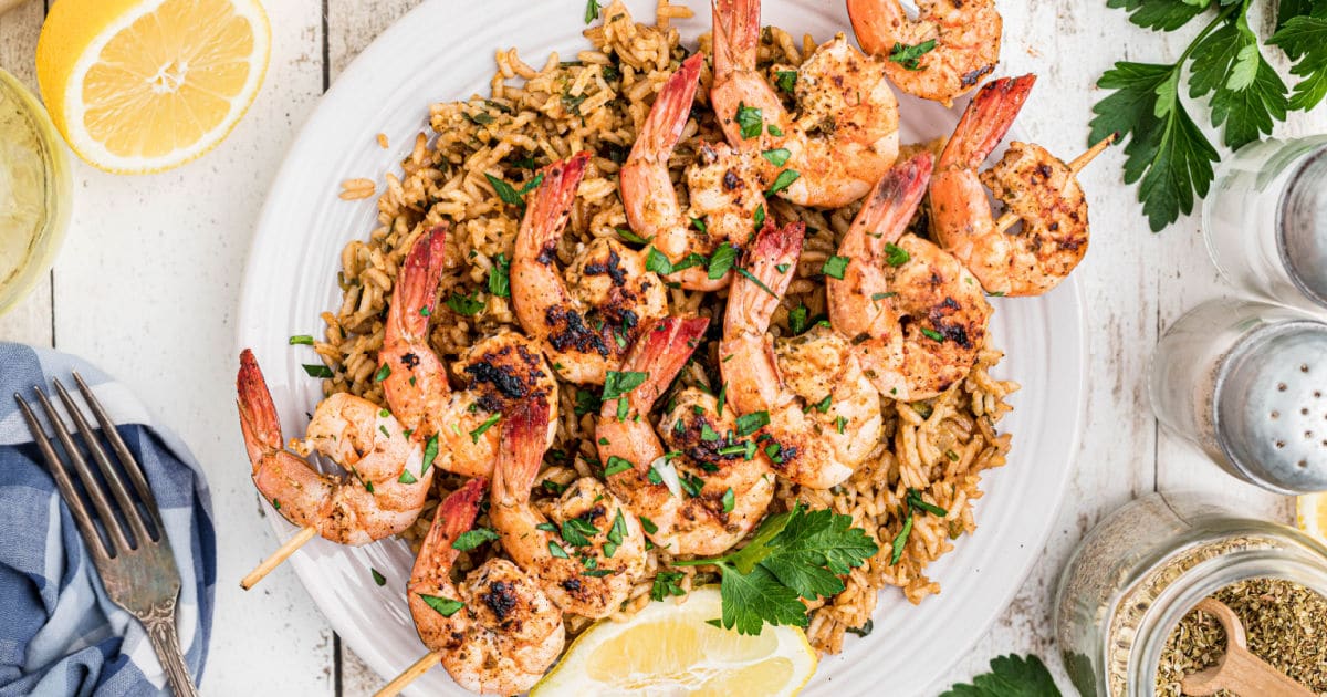 a plate of seasoned rice with some grilled shrimp kabobs sitting on top