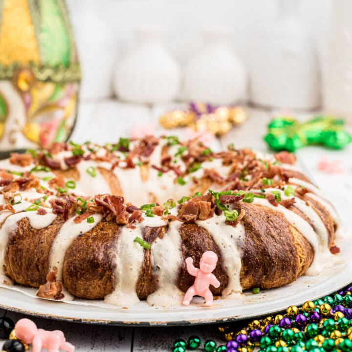 close up from the side of a boudin king cake with a king cake baby in front and some mardi gras stuff in the background