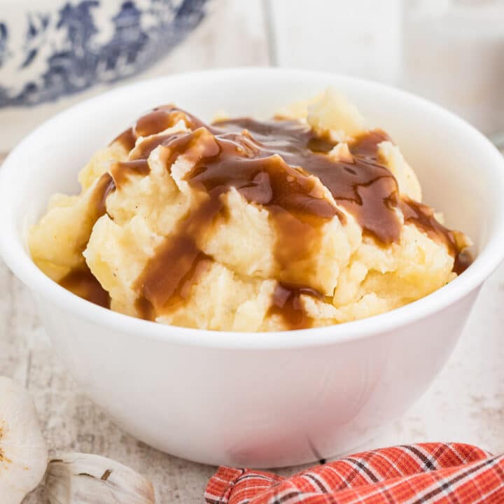 A bowl full of mashed potatoes with brown gravy on top.