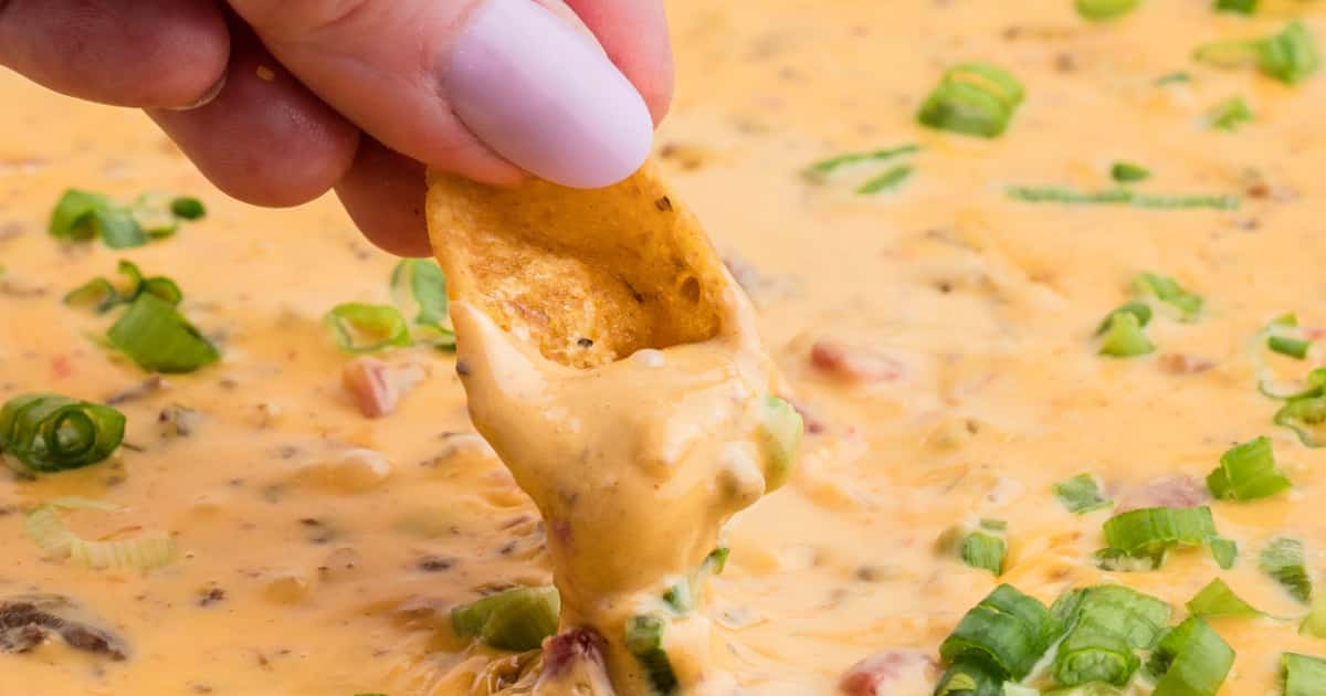 someone using a corn chip to dip into a large tray of smoked queso dip.