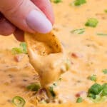 close up of someone's fingers dipping a chip into smoked queso dip
