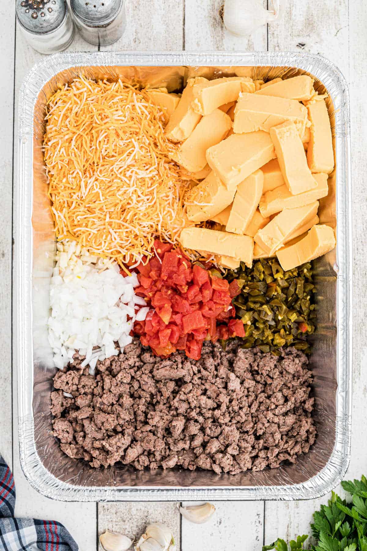 overhead shot of a foil pan full of smoked queso dip ingredients
