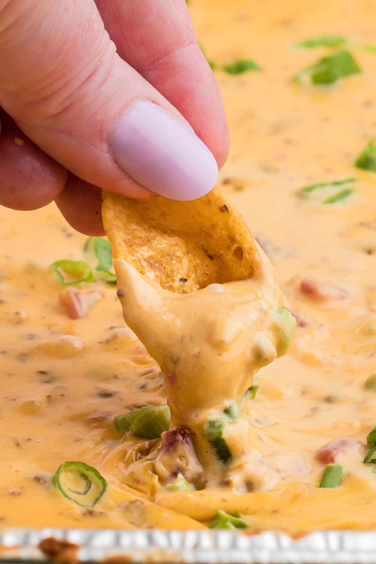 close up of someone's fingers dipping a chip into smoked queso dip