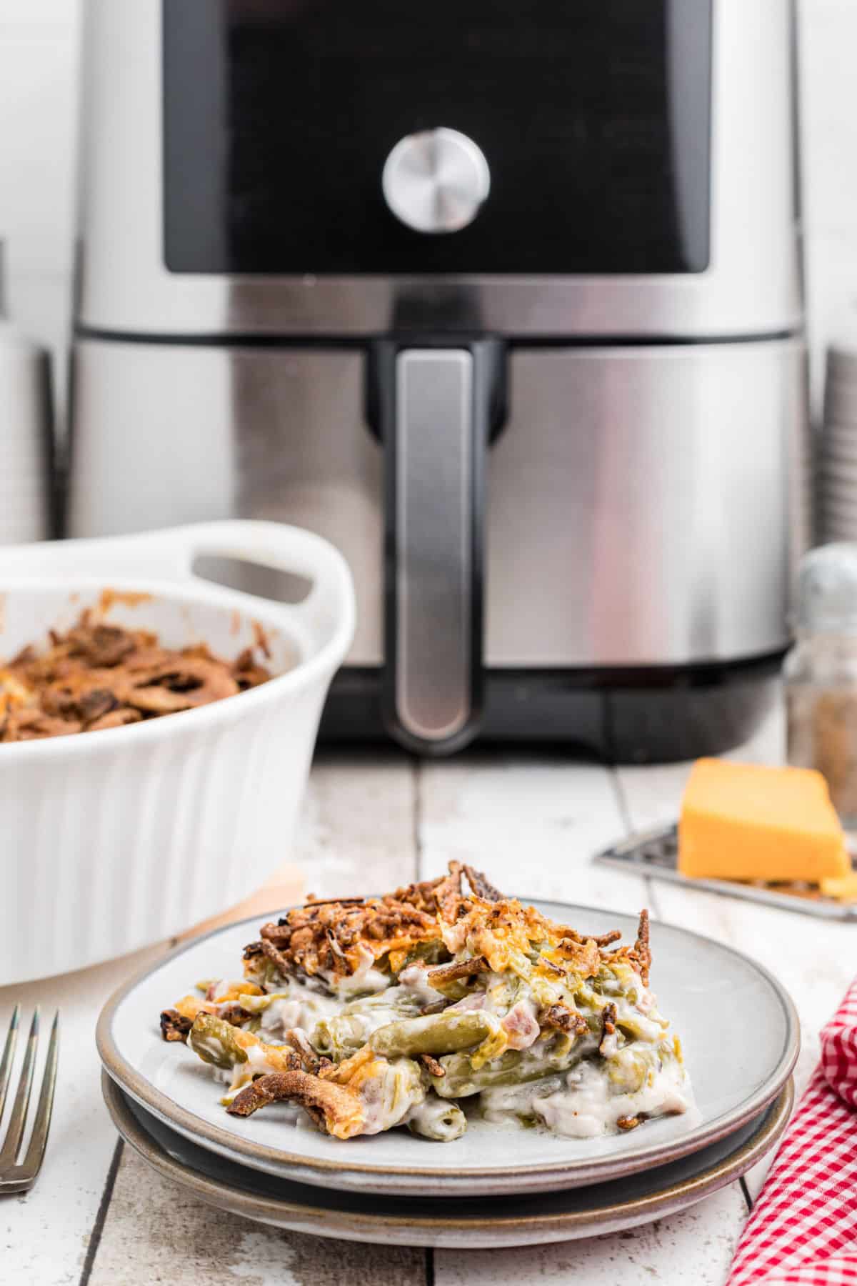 A dish with a serving of green bean casserole in front of an air fryer.