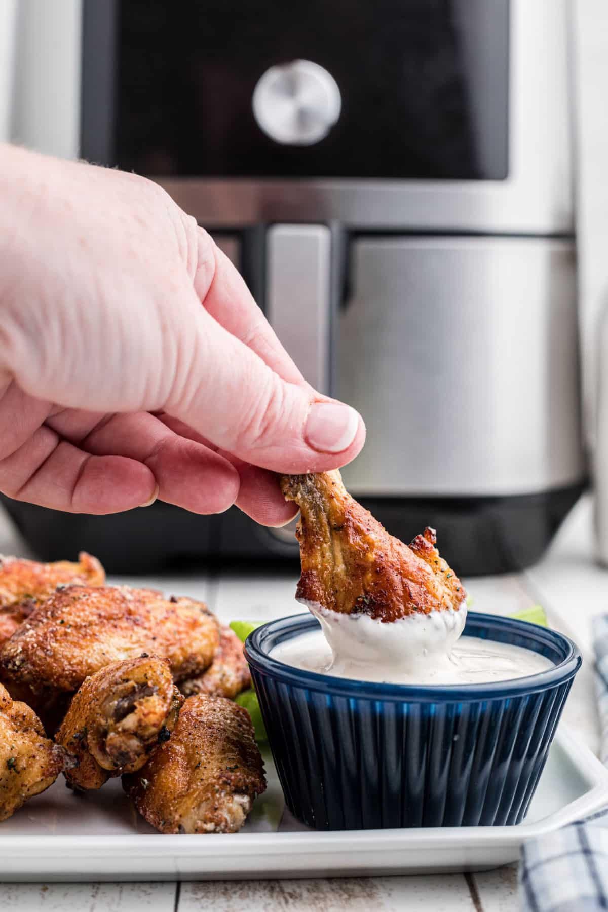 A hand dipping an air fried ranch chicken wing into some dip.
