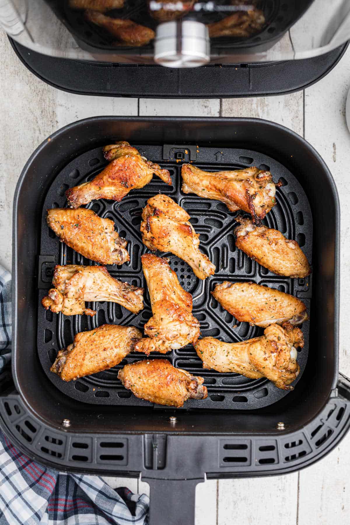 An air fryer basket with some ranch chicken wings cooked inside.
