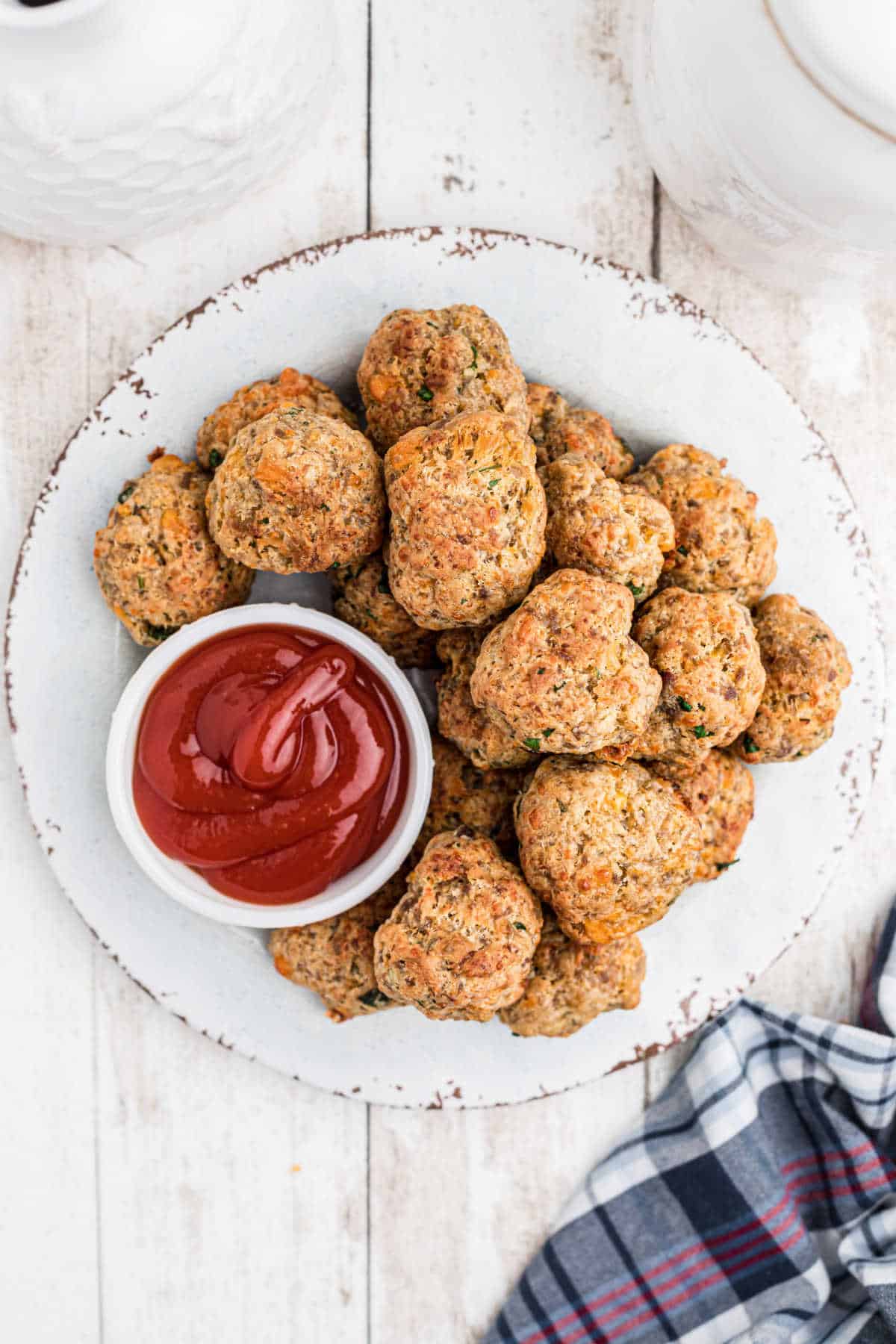 Overhead shot of a plate full of air fryer sausage balls and a small bowl of ketchup.