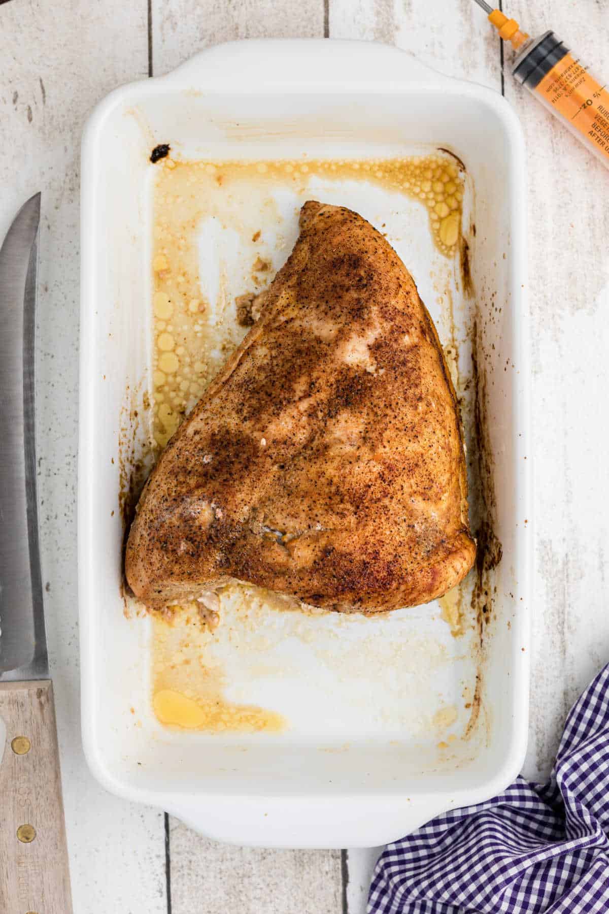 A cooked and seasoned turkey breast in a baking dish.
