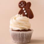 A cupcake with cream cheese frosting on top with a gingerbread man sticking out the top.