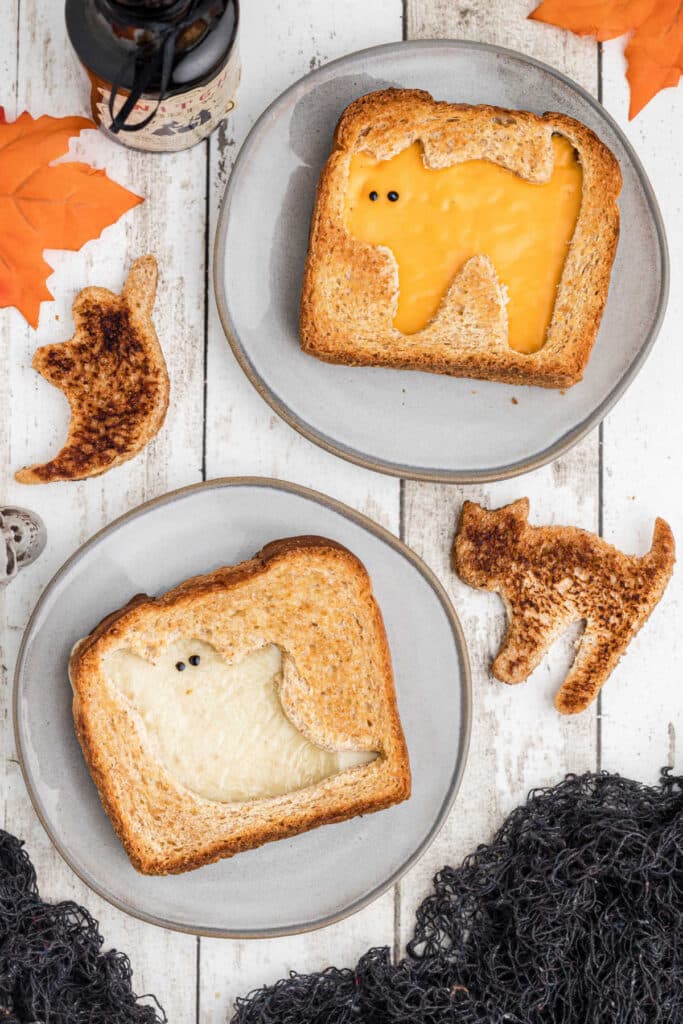 Two plates with halloween grilled cheese sandwiches, one cat one ghost.