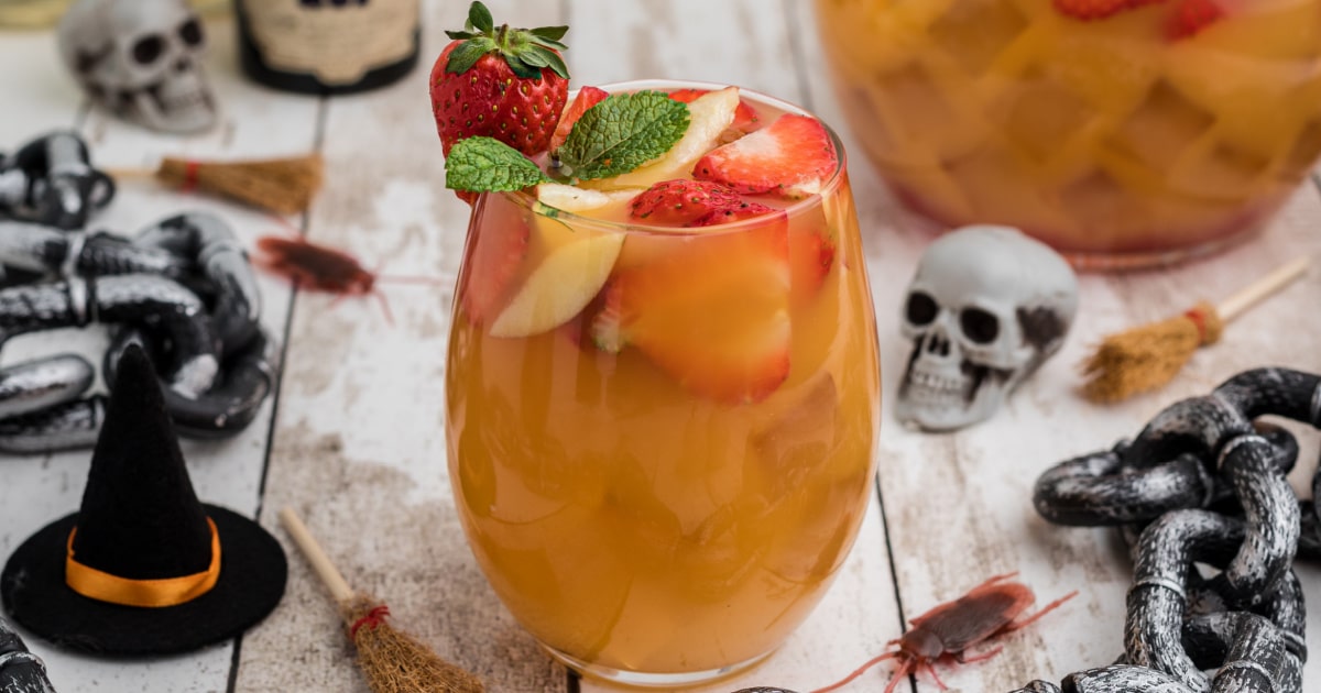 a glass of halloween jungle juice with fruit in the top with halloween decorations.