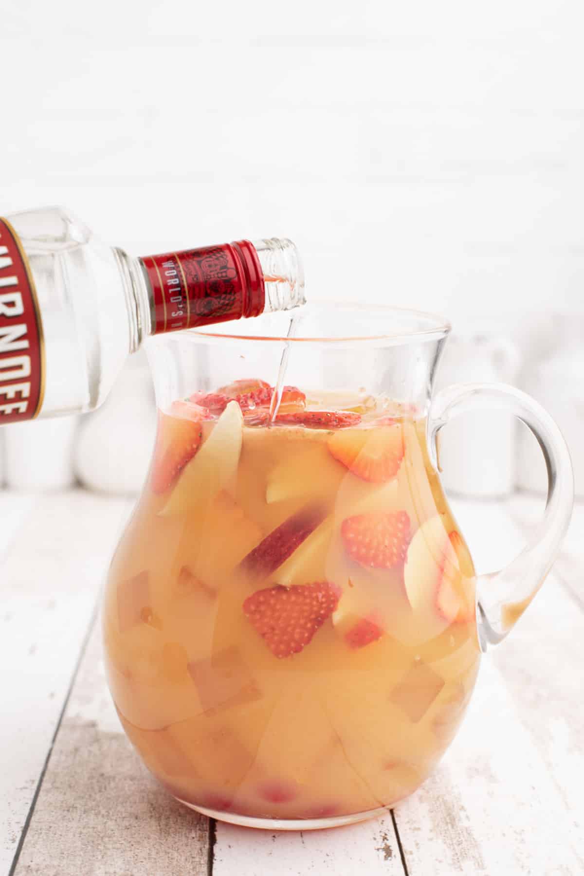 A large pitcher of jungle juice with fruit pieces in it.