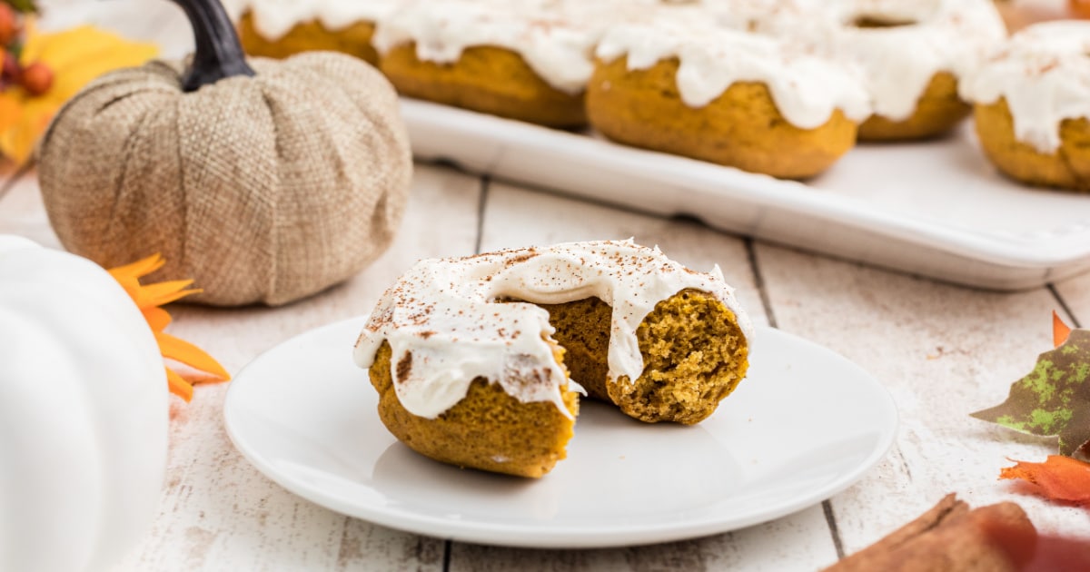 a close up of a pumpkin spice donut with cream cheese frosting, with a bite taken.