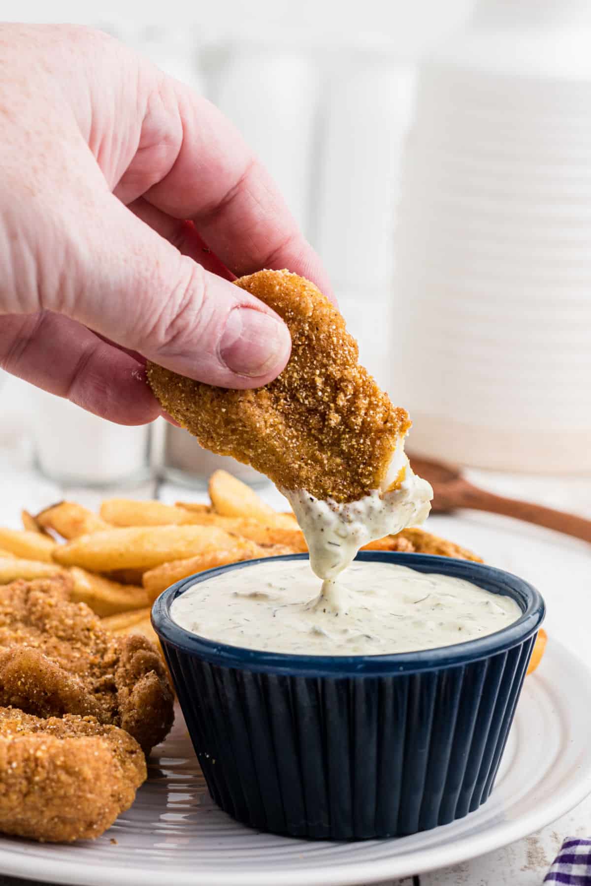 A piece of fish being dipped into some southern tartar sauce.