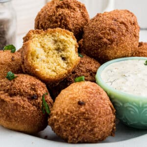 Some sweet hush puppies on a plate with a bite taken out of one, with a dip.