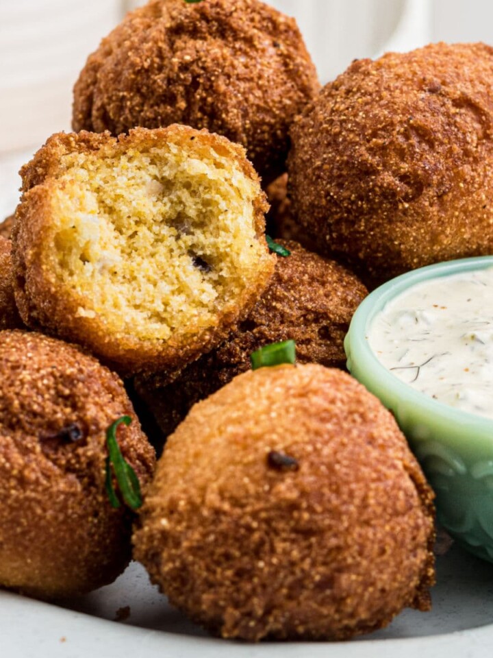 Some sweet hush puppies on a plate with a bite taken out of one, with a dip.