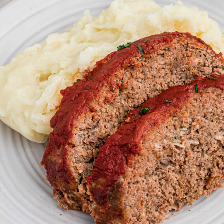 Close up shot of two slices of venison meatloaf against some mashed potatoes.
