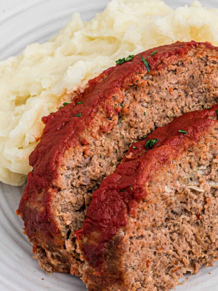 Close up shot of two slices of venison meatloaf against some mashed potatoes.