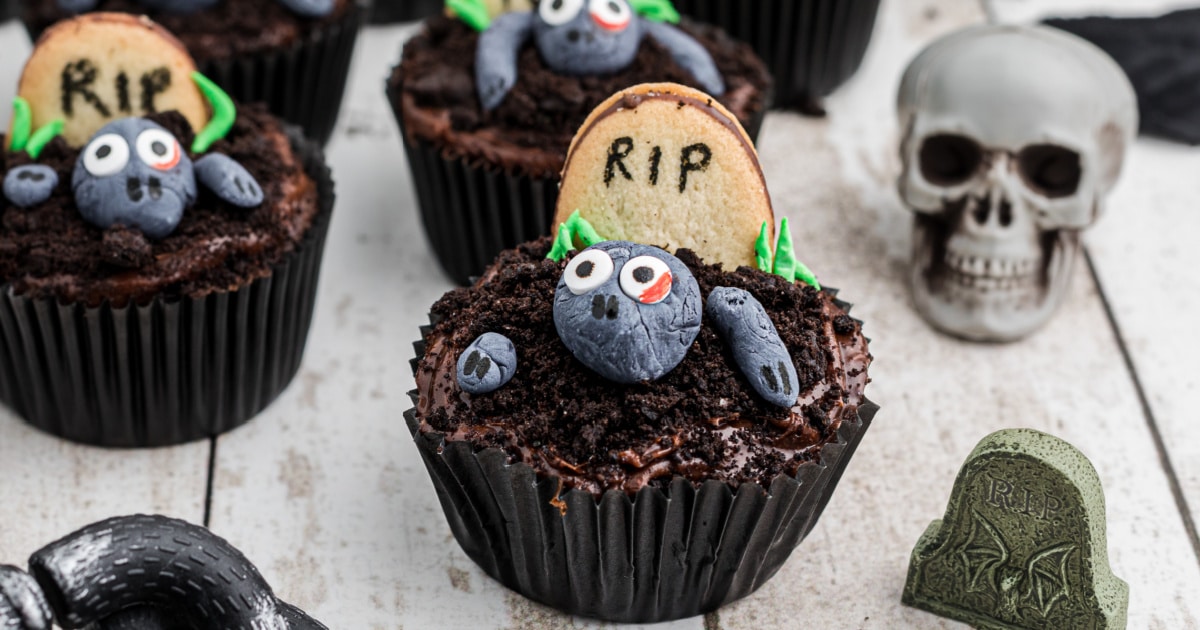 A chocolate cupcake with a zombie coming out of the earth with a cookie headstone.