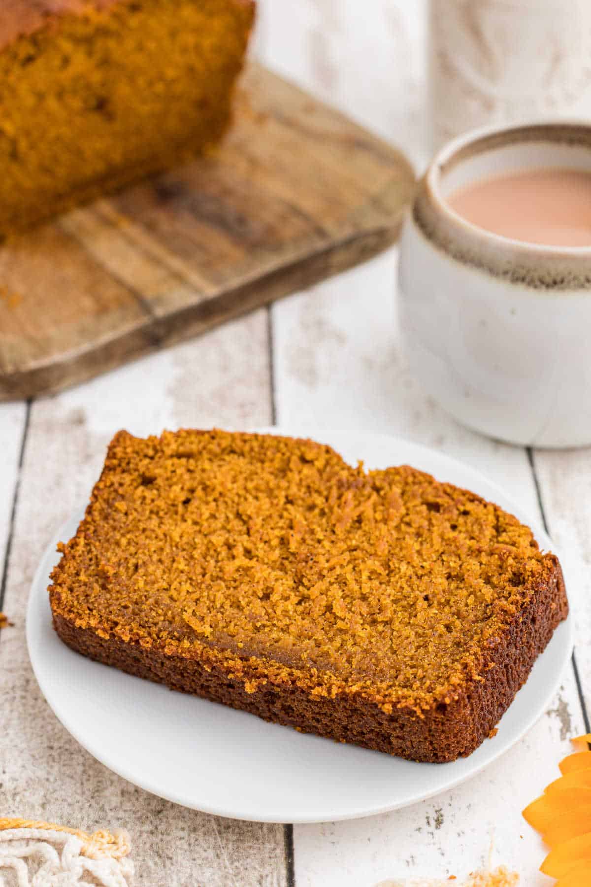 A slice of Amish Pumpkin Bread on a white plate with a coffee behind it.
