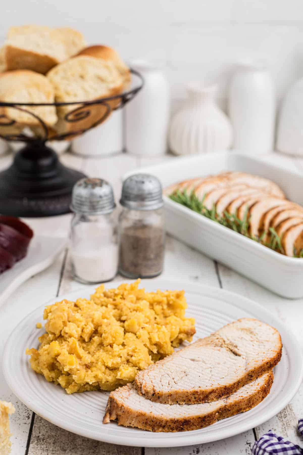 Sliced cajun turkey breast on a plate with some corn casserole.