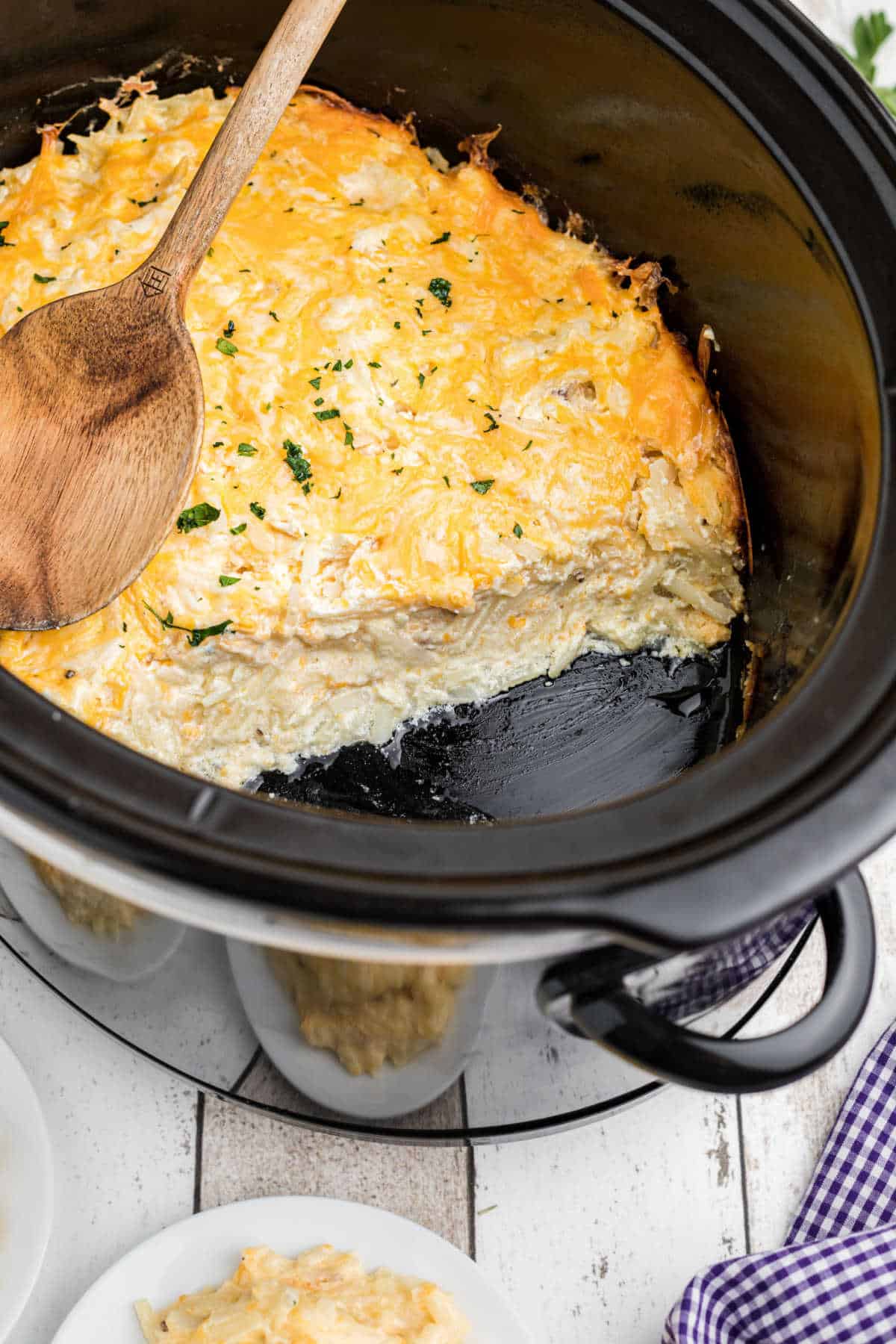 another image showing cheesy crock pot hash brown casserole with a bunch gone and a spoon resting on top.