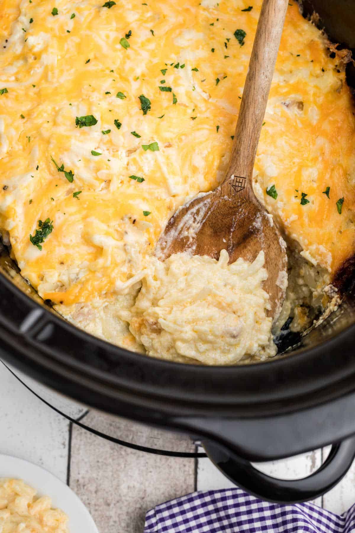 A crockpot full of cracker barrel hash brown casserole with a spoon digging in.