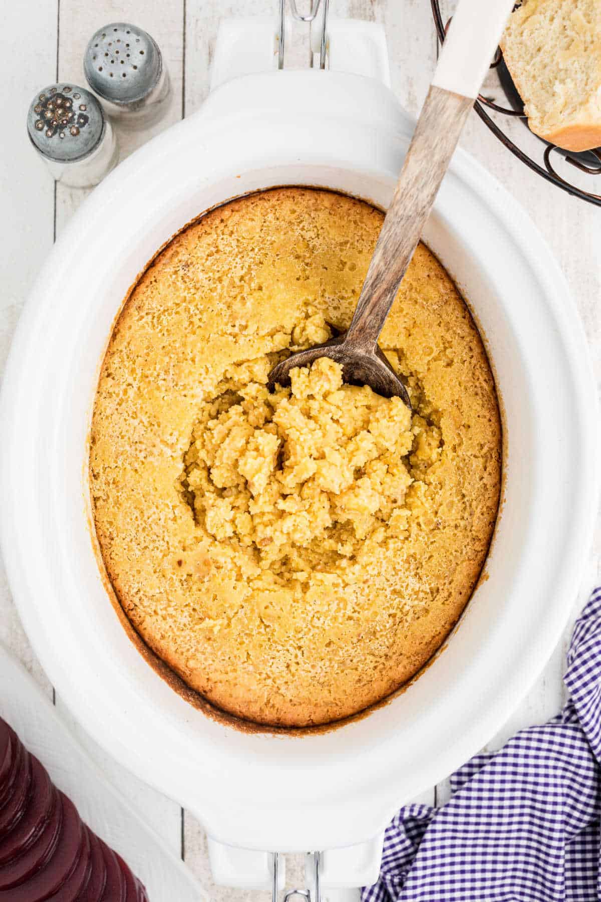 A spoon resting on a jiffy corn casserole in a crock pot.