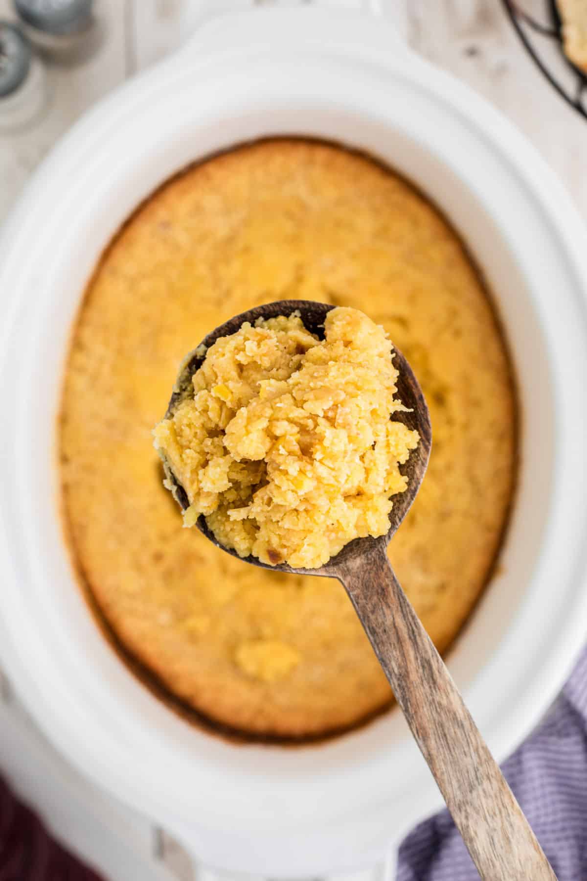 A spoon full of corn casserole being lifted out of a crock pot.