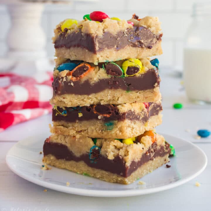Close up of a stack of M&M Chocolate oat bars with a glass of milk in the background.