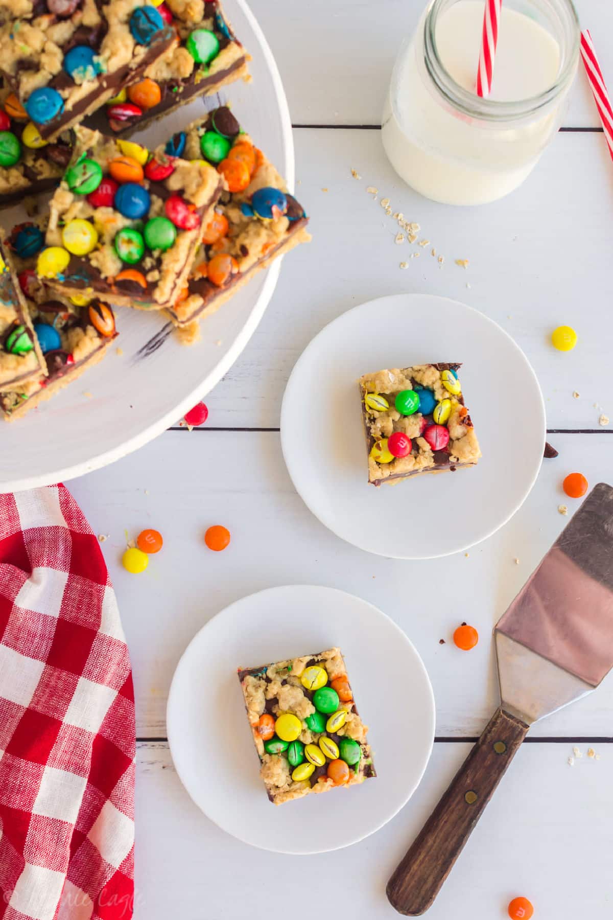 two plates with an M&M chocolate oat bar on each, with a cake stand filled with them.