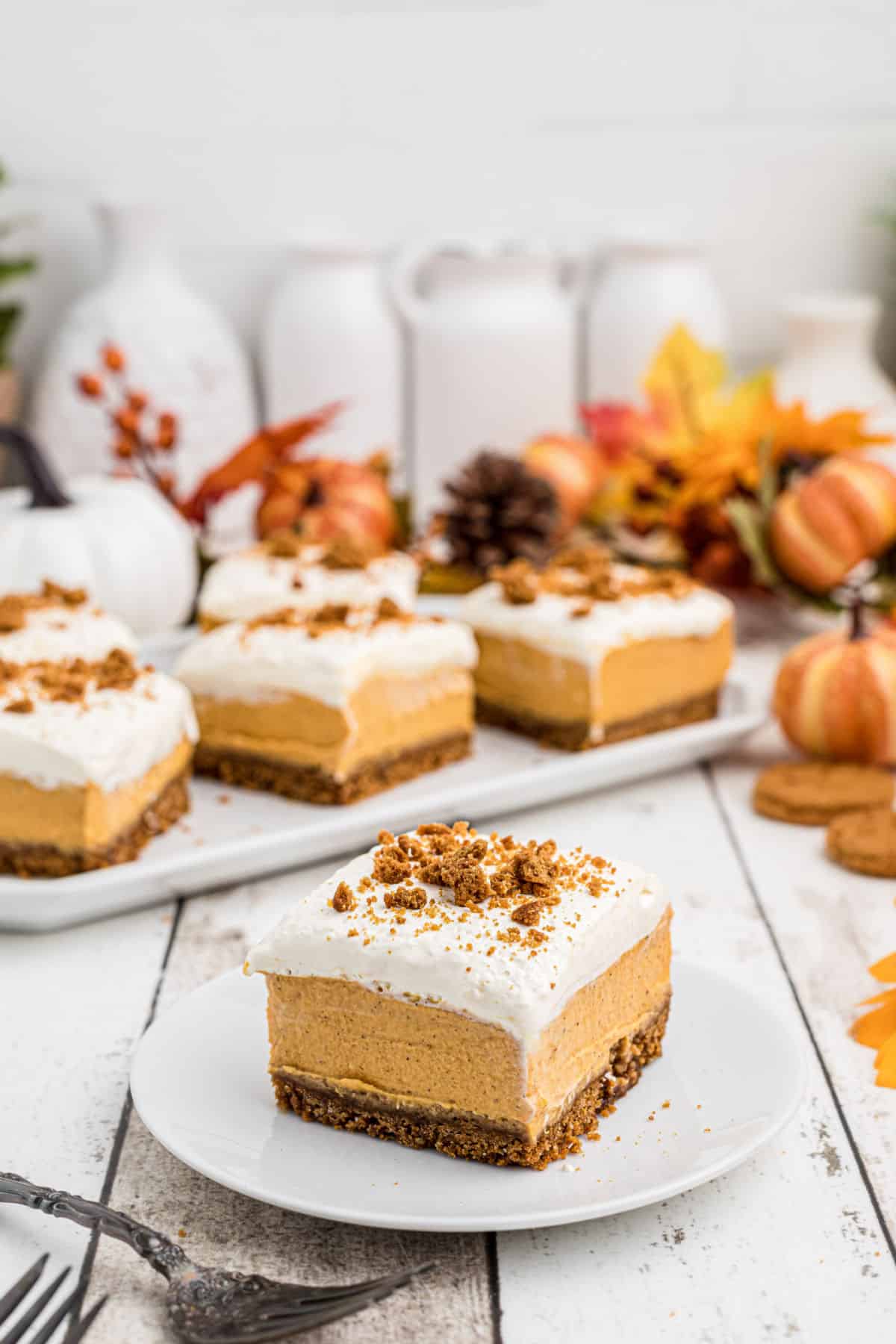 A slice of no bake pumpkin cheesecake bars on a plate in front of a serving plate of them.